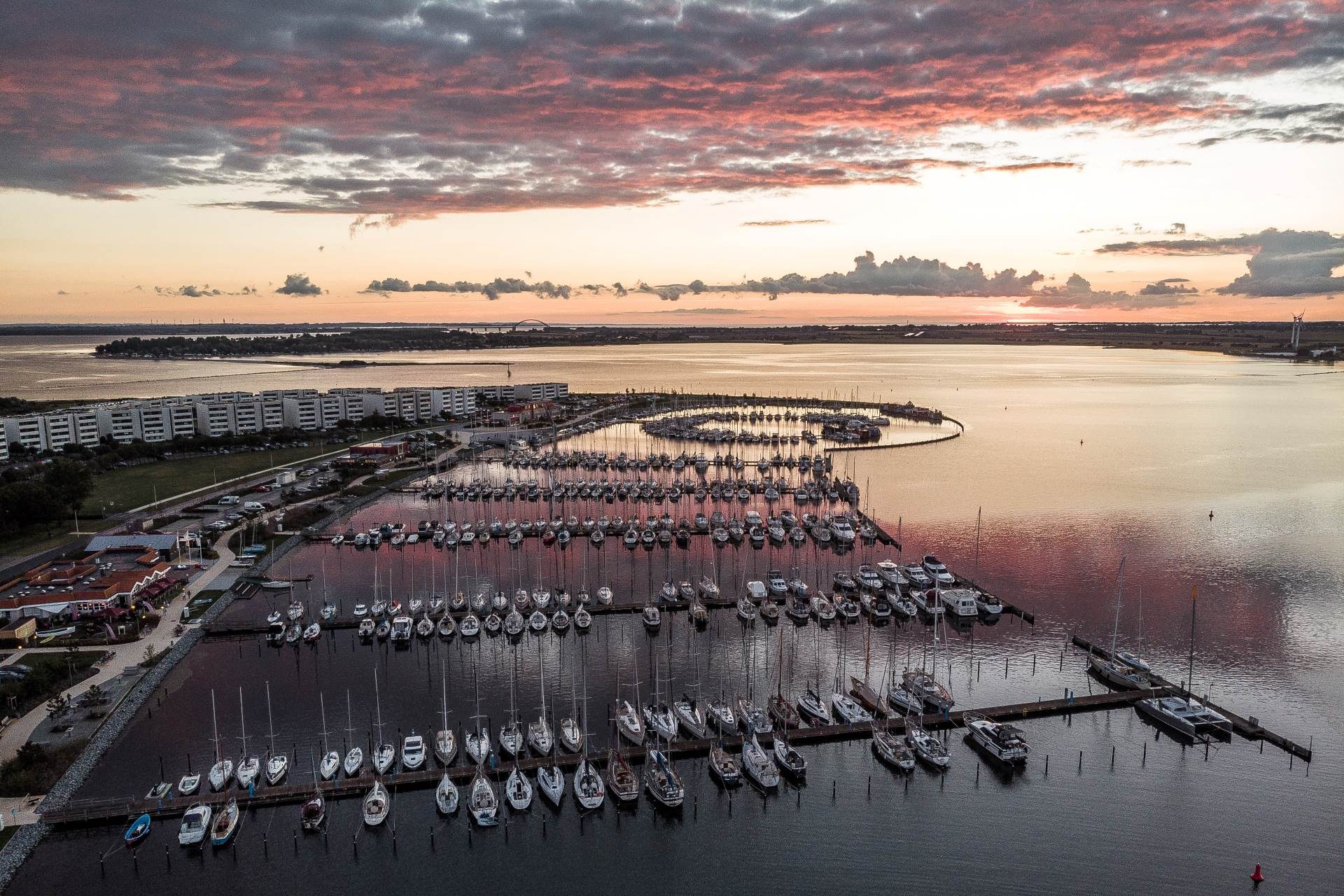 Drohnenfoto eines Yachthafens auf Fehmarn, im Hintergrund geht die Sonne unter. 